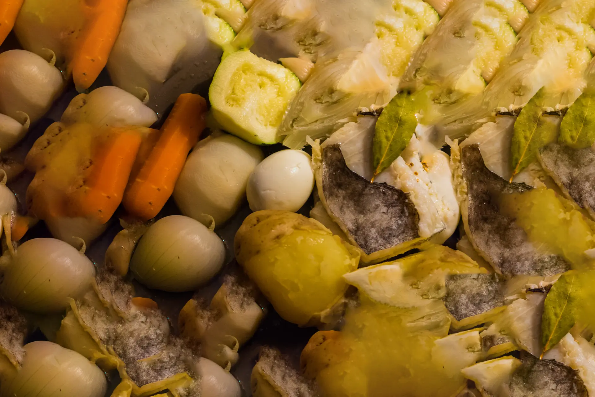 La photo montre une assiette de nourriture composée d’œufs durs, de pommes de terre, de carottes et de ce qui semble être des tranches de poisson. Les aliments sont disposés sur une nappe à motifs circulaires avec des couleurs chaudes comme l’orange, le jaune et le marron.