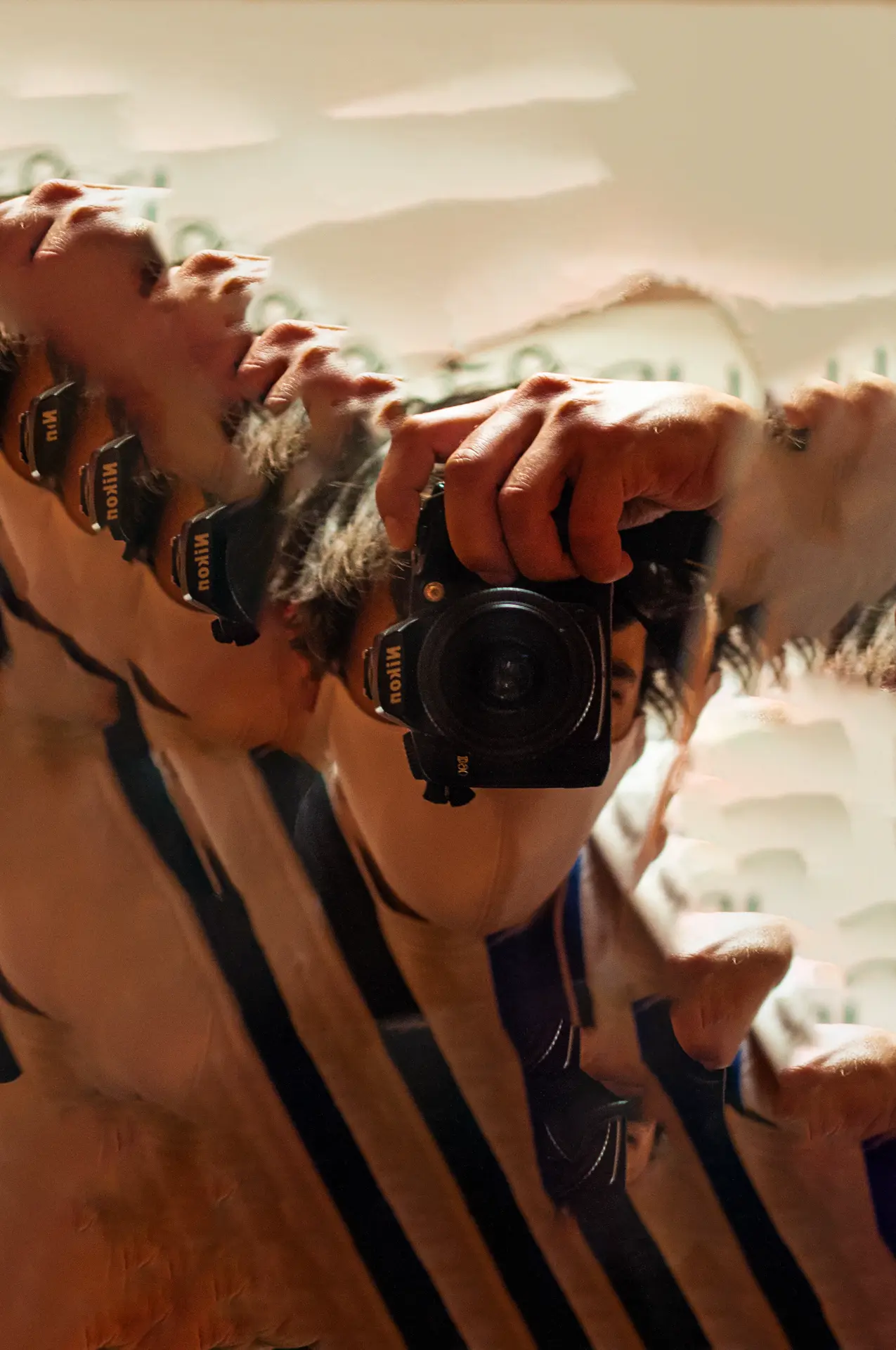 Cette photo montre un autoportrait dans un miroir brisé. L’artiste est visible à travers un fragment central du miroir, tenant un appareil photo Nikon dirigé vers lui-même, capturant son reflet. Le miroir est entouré de morceaux colorés en jaune, orange, rouge, et bleu, évoquant un vitrail ou une mosaïque. Les contours irréguliers des éclats de verre créent une fragmentation de la scène, tandis que la main tenant l’appareil occupe une position dominante, ajoutant une touche de mouvement et d’ombre. Techniquement, l’image utilise une faible profondeur de champ, avec un flou sur les bords colorés et une mise au point nette sur l’appareil photo et la main, ce qui guide l’œil vers le sujet principal. Symboliquement, le miroir brisé peut évoquer des thèmes de l'identité, de la multiplicité et de la perception fragmentée de soi. Cela rappelle les œuvres de photomontage et les compositions cubistes qui déconstruisent la réalité. Historiquement, l’autoportrait dans le miroir est un classique de la photographie, mais ici, l’utilisation du miroir brisé renouvelle le concept en y ajoutant une dimension introspective et poétique, rappelant les questionnements modernes sur la construction de l’image de soi.